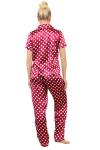 Model wearing a fuchsia satin polka dot pyjama set featuring a short-sleeve button-up top and matching full-length pants, showcasing a stylish and comfortable loungewear option.