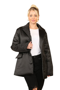 Woman wearing a black satin puffer jacket with a buckle belt, double-breasted closure, and buttoned pockets, styled for a chic streetwear look