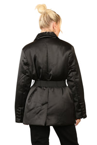 Woman wearing a black satin puffer jacket with a buckle belt, double-breasted closure, and buttoned pockets, styled for a chic streetwear look